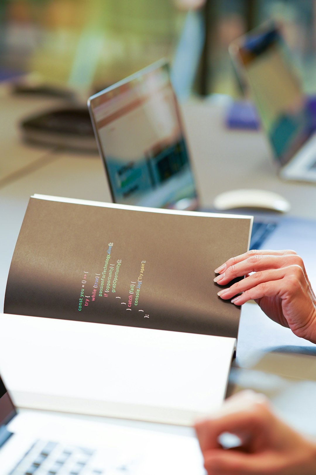 A programmers notebook with code written on it in a meeting room with laptops.